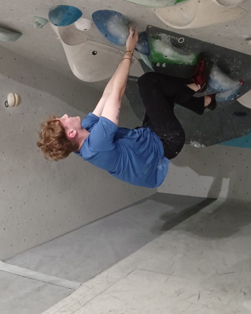 Kollege mit blauem Shirt beim Bouldern